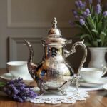 Hamsa silver teapot moroccan with hand-engraved patterns on lace doily with glass cups and lavender