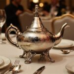 Silver teapot circular medallion engraved on a dining table with Moroccan glasses and traditional snacks