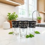 Three elegant black pattern tea glasses accented with hand-painted silver details, beautifully displayed on a bright white quartz kitchen countertop alongside fresh mint leaves.