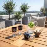 Sunlit black pattern tea glasses resting on a wooden patio table in a scenic rooftop setting, styled with a glass pitcher of fresh mint water and a small bowl of sugar cubes.