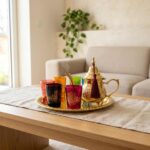 Steaming hot gold brass hamsa tea set resting gracefully on a light beige linen runner over a wooden coffee table, situated in a cozy, bright modern living room setting.