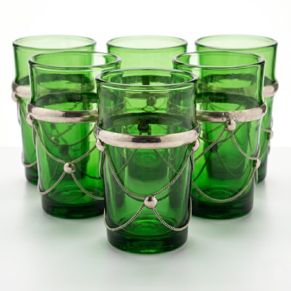 Six green beldi tea glasses with silver filigree chain-wrap metal holders on white background