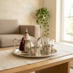 Steaming hot hand-hammered silver plated tea set resting gracefully on a light beige linen runner over a wooden coffee table, situated in a bright, modern living room setting.