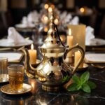 A handcrafted brass teapot with a polished gold finish sits on a black marble table in a luxury restaurant setting, surrounded by glowing candles, traditional tea glasses, and fresh mint.