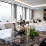Minimalist hammered silver teapot on dark marble with gold tea glasses and fresh mint leaves