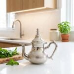 Minimalist hammered silver teapot on white quartz countertop in a bright kitchen with green accents