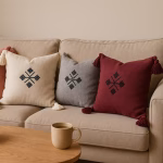 Collection of four Moroccan boho cushions in coral, cream, gray, and burgundy with corner tassels and traditional embroidered patterns, styled on a neutral sofa with natural wood coffee table