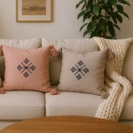 Cozy living space featuring three Moroccan boho cushions in cream, coral, and light beige with matching tassels and geometric embroidery, arranged on a light sofa with chunky knit throw