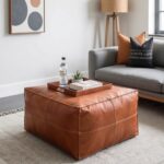 Square leather ottoman in cognac brown used as coffee table with tray in contemporary living room