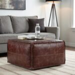Distressed brown square leather ottoman with visible patina and stitching on neutral surface