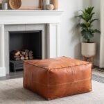 Cognac square leather ottoman pouf in modern living room near white fireplace with greenery