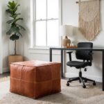 Large cognac square leather ottoman at foot of bed in modern bedroom with gray linens
