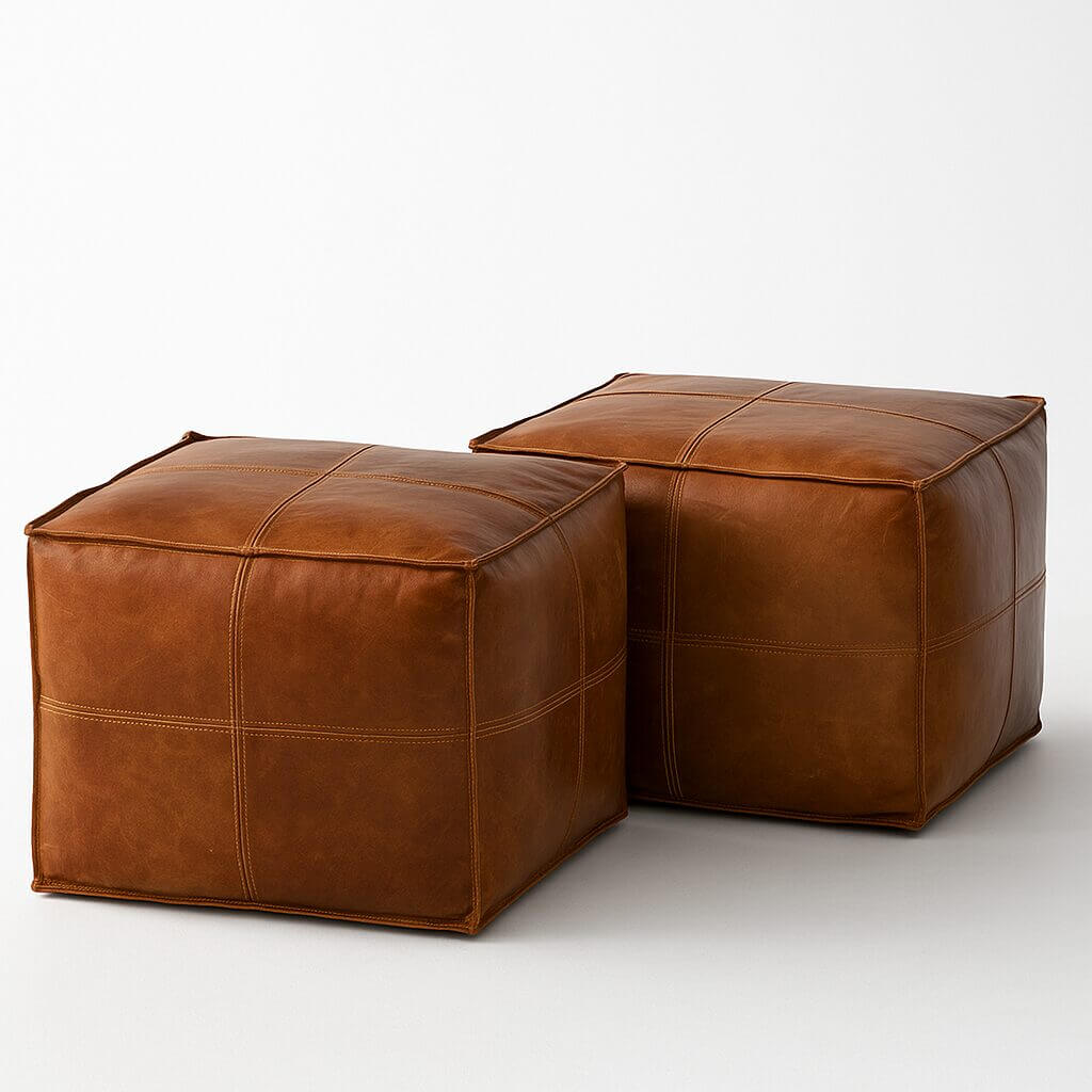 Product shot of two matching square leather poufs Square leather ottoman set of 2 handcrafted brown poufs with white stitching detail on white background