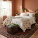 Dark brown leather kilim cube ottoman at foot of bed in warm terracotta bedroom with Persian rug and white linens