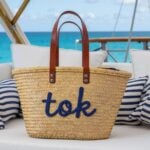 Personalized straw bag with navy cursive embroidery on boat cushion, handwoven palm leaf and tan leather handles