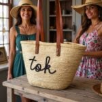 Personalized straw bag with black cursive embroidery displayed by two women, handwoven palm leaf and leather straps