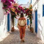 Woman wearing a Convertible Straw Backpack Tote as a backpack while walking through a Mediterranean cobblestone street with bougainvillea