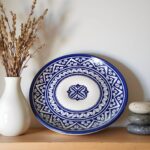 Hand-painted blue ceramic plates with intricate geometric patterns displayed on wooden shelf with dried flowers