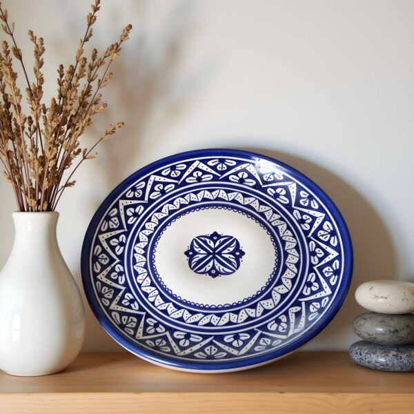 Hand-painted blue ceramic plates with intricate geometric patterns displayed on wooden shelf with dried flowers