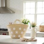 Star straw bag on white kitchen counter beside white pitcher and flowers, beige handwoven tote with white star appliqué