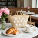 Star straw bag on white marble table with croissants coffee and pink peonies, beige handwoven market tote