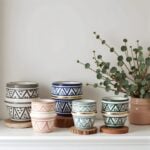 Handmade ceramic cups with gold rim and geometric patterns displayed with eucalyptus on white shelf