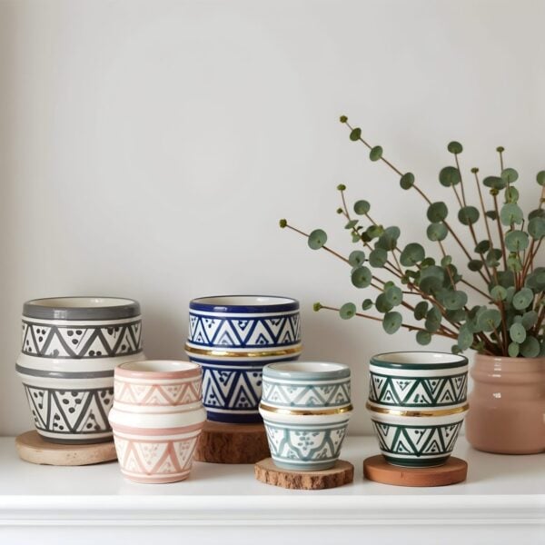 Handmade ceramic cups with gold rim and geometric patterns displayed with eucalyptus on white shelf