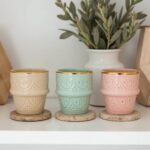 Ceramic espresso cups with geometric relief patterns and gold trim on textured coasters
