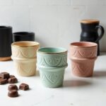 Set of ceramic espresso cups with gold ornaments in pastel colors displayed with chocolate treats