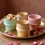 Ceramic espresso cups in beige, mint, and pink with intricate relief patterns and gold accents