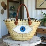Handwoven straw evil eye beach bag with nazar embroidery displayed on whitewashed wooden table