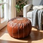 Leather floor ottoman near a glass door, positioned next to an armchair with a grey knit blanket.