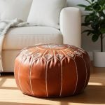Sunlit leather floor ottoman sitting on a wooden floor next to a modern white sofa.