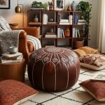 Dark brown leather floor ottoman in a bohemian living room surrounded by floor pillows, a leather armchair, and books.