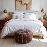 Dark brown leather floor ottoman placed at the foot of a bed with white linens and wooden nightstands.