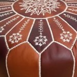 Macro close-up of the white geometric embroidery on the top of a dark brown leather floor ottoman.