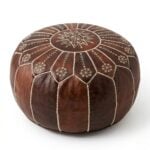 A dark brown leather floor ottoman featuring intricate white embroidered geometric patterns, isolated against a solid white background.