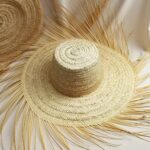 Flat lay of handmade straw accessories hat displaying circular basketweave pattern and radiating natural raffia fringe