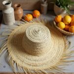 Lifestyle shot of handcrafted straw accessories hat with oranges and ceramic vases on rustic table setting