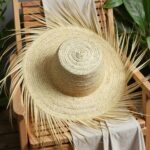 Natural straw accessories beach hat displayed on wooden chair showing bohemian fringe and wide brim construction
