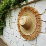 Natural straw hat with fringe against white wall