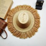Hand touching handwoven straw garden hat with fringe, detailed spiral weave craftsmanship, natural fibers