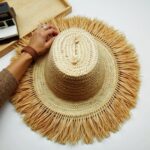 Handwoven straw garden hat with fringe on wooden table, ceramic bowl, rustic home decor styling