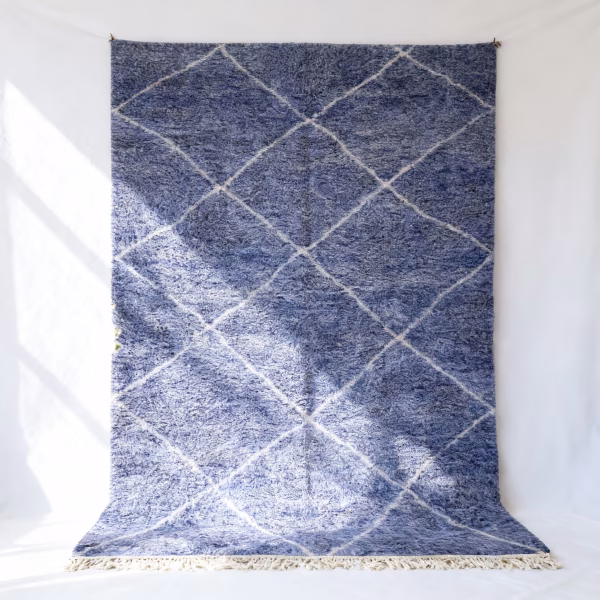 Authentic Moroccan farmhouse rug in blue with white diamond lattice pattern and cotton fringe hanging on white wall