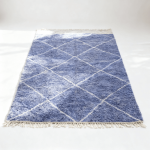 Handwoven blue farmhouse rug with diamond lattice design and cream fringe on white floor