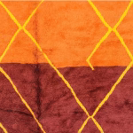 Close-up of orange and burgundy wool sections with yellow diamond patterns on handmade Moroccan rug