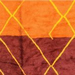 Close-up of orange and burgundy wool sections with yellow diamond patterns on handmade Moroccan rug