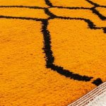 Close-up texture of Moroccan rug showing hand-knotted orange wool pile with black geometric pattern detail