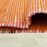 Underside of handwoven Moroccan rug revealing traditional striped weaving technique in pink orange and cream tones