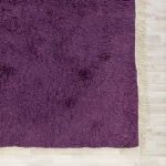 Detail view of purple section of handmade colorful Moroccan wool rug with edge fringe
